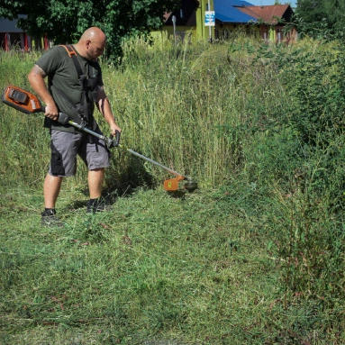 Hausmeister mäht hohes Gras mit Freischneider
