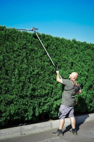 Hausmeister schneidet hohe Hecke mit Teleskop-Heckenschere